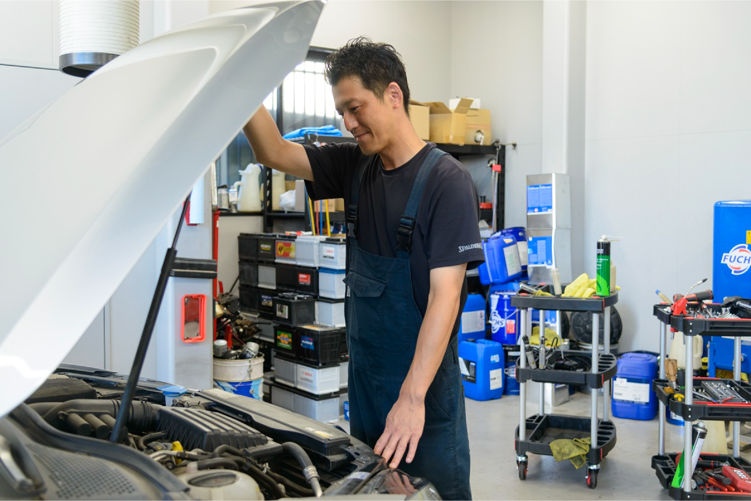 青いツナギを着た男性が車のボンネットを開けている写真