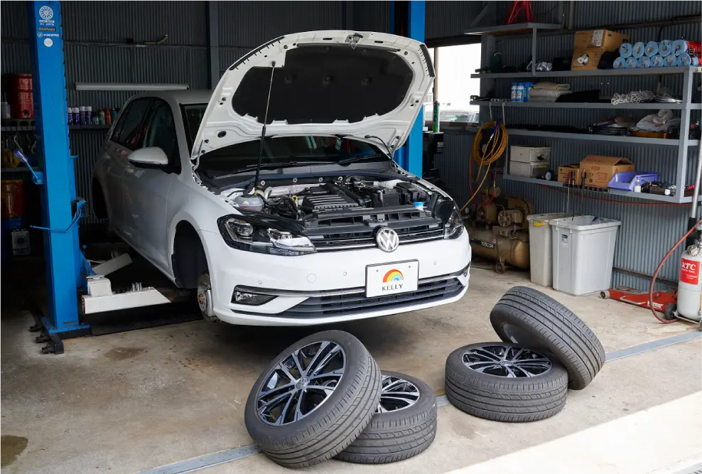 工場内でボンネットが開かれた車と積まれたタイヤの写真