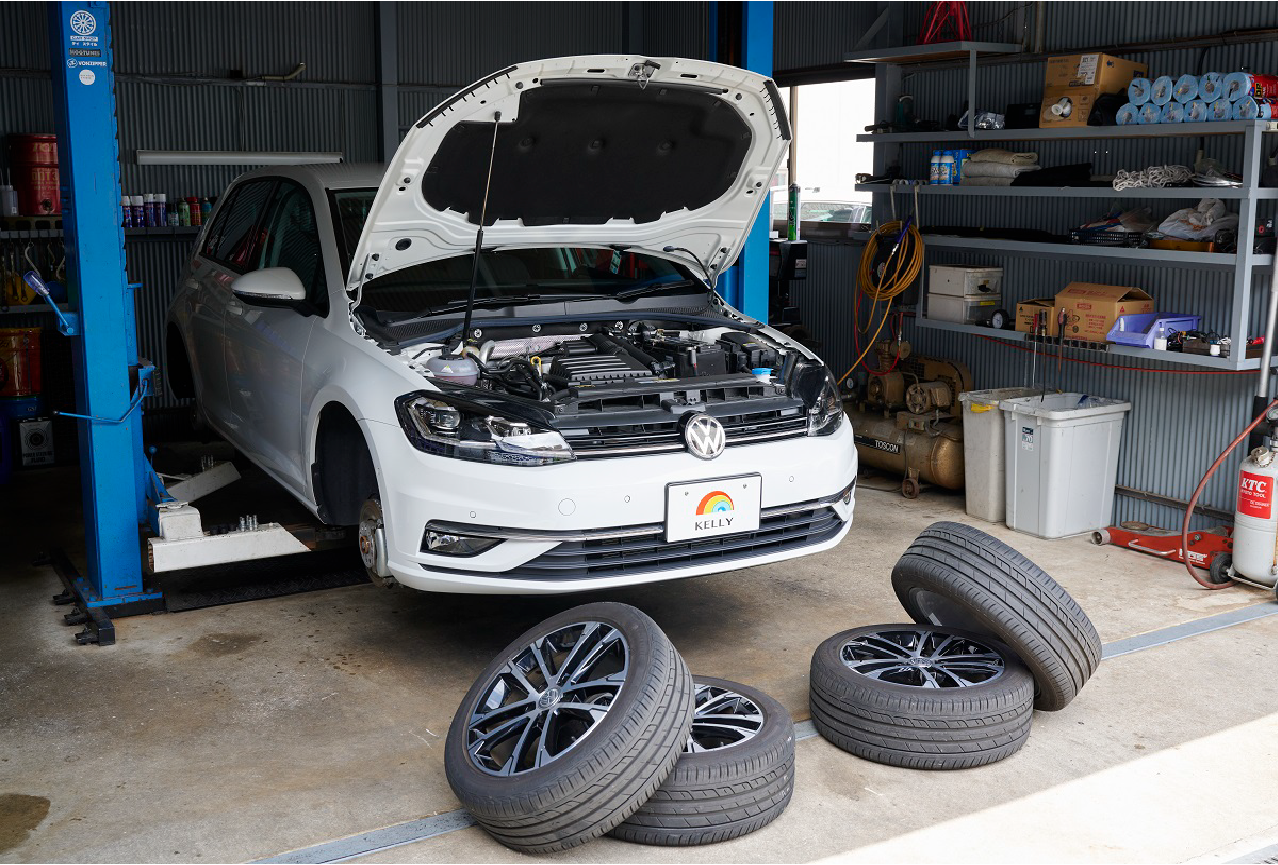 工場内でボンネットが開かれた車と積まれたタイヤの写真