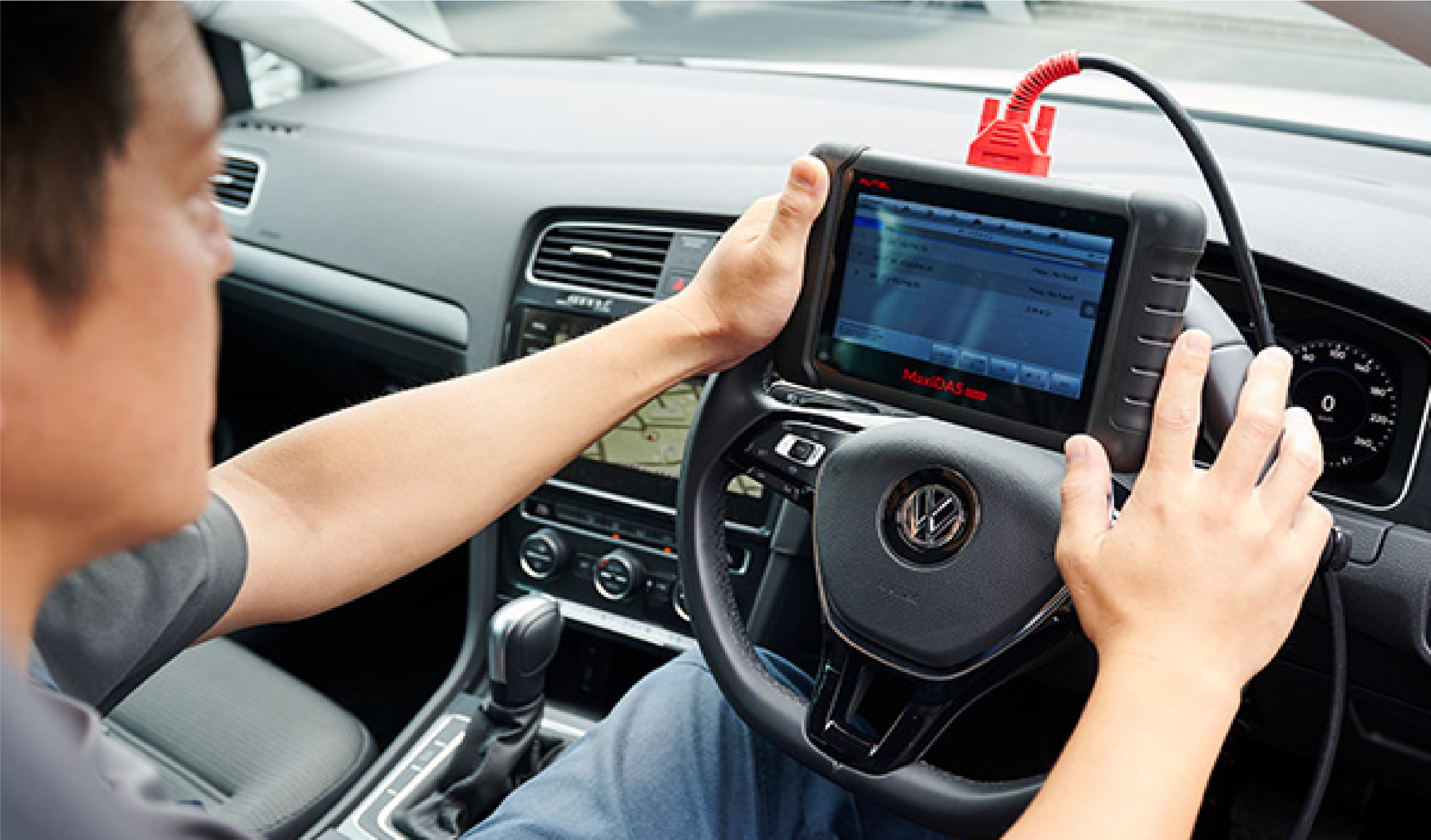 車に繋がった自動車の故障診断機診断機MaxiSysの画面を確認している様子の写真